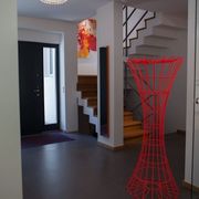 Blick in einen Eingangsbereich mit Deckenleuchte, Treppenaufgang und roter Stehlampe